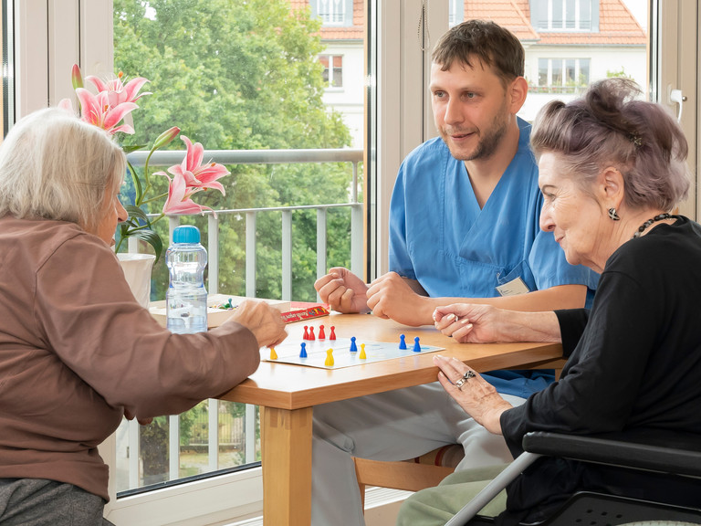 Pflegekraft spielt Mensch ärgere dich nicht mit Bewohnerinnen - Immanuel Seniorenzentrum Schöneberg