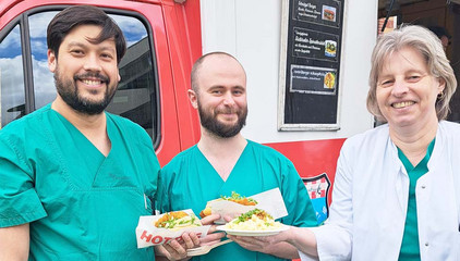 Zwei Pflegekräfte in blauer Funktionskleidung eine Ärztin in weißer Funktionskleidung stehen mit Essen in den Händen vor einem Food-Truck am Internationalen Tag der Pflegenden im Immanuel Klinikum Bernau Herzzentrum Brandenburg. Zwei Pflegekräfte in blauer Funktionskleidung eine Ärztin in weißer Funktionskleidung stehen mit Essen in den Händen vor einem Food-Truck am Internationalen Tag der Pflegenden im Immanuel Klinikum Bernau Herzzentrum Brandenburg.