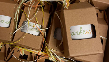 Mehrere in einer Kartonverpackung mit Sichtfenster verpackte weiße Tassen mit einer Aufschrift "Dankeschön" als grün-orangene Bändergrafik als Geschenk für Pflegekräfte am Internationalen Tag der Pflegenden. Mehrere in einer Kartonverpackung mit Sichtfenster verpackte weiße Tassen mit einer Aufschrift "Dankeschön" als grün-orangene Bändergrafik als Geschenk für Pflegekräfte am Internationalen Tag der Pflegenden.